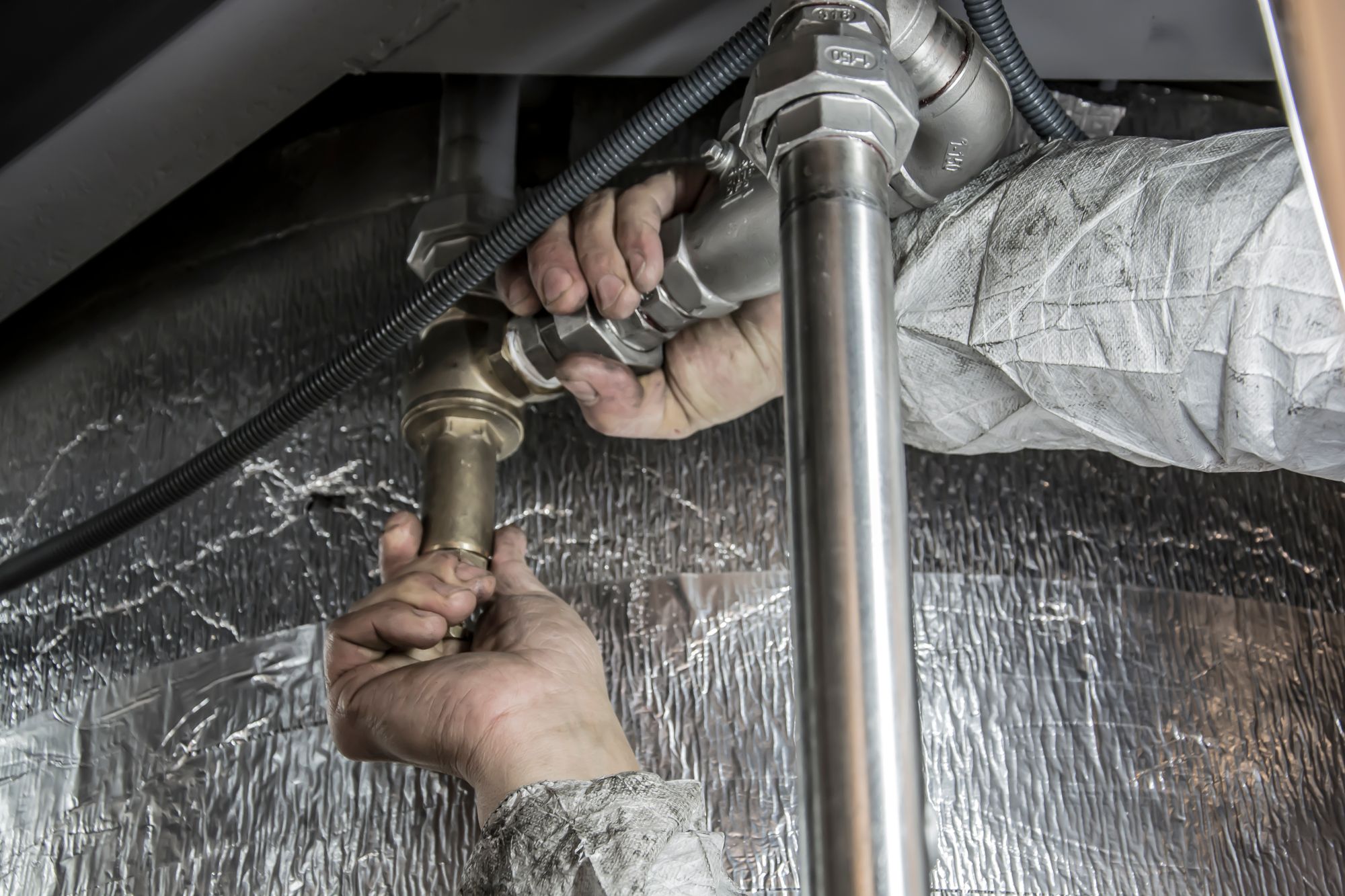 Plumber fitting metal pipes beneath a fixture